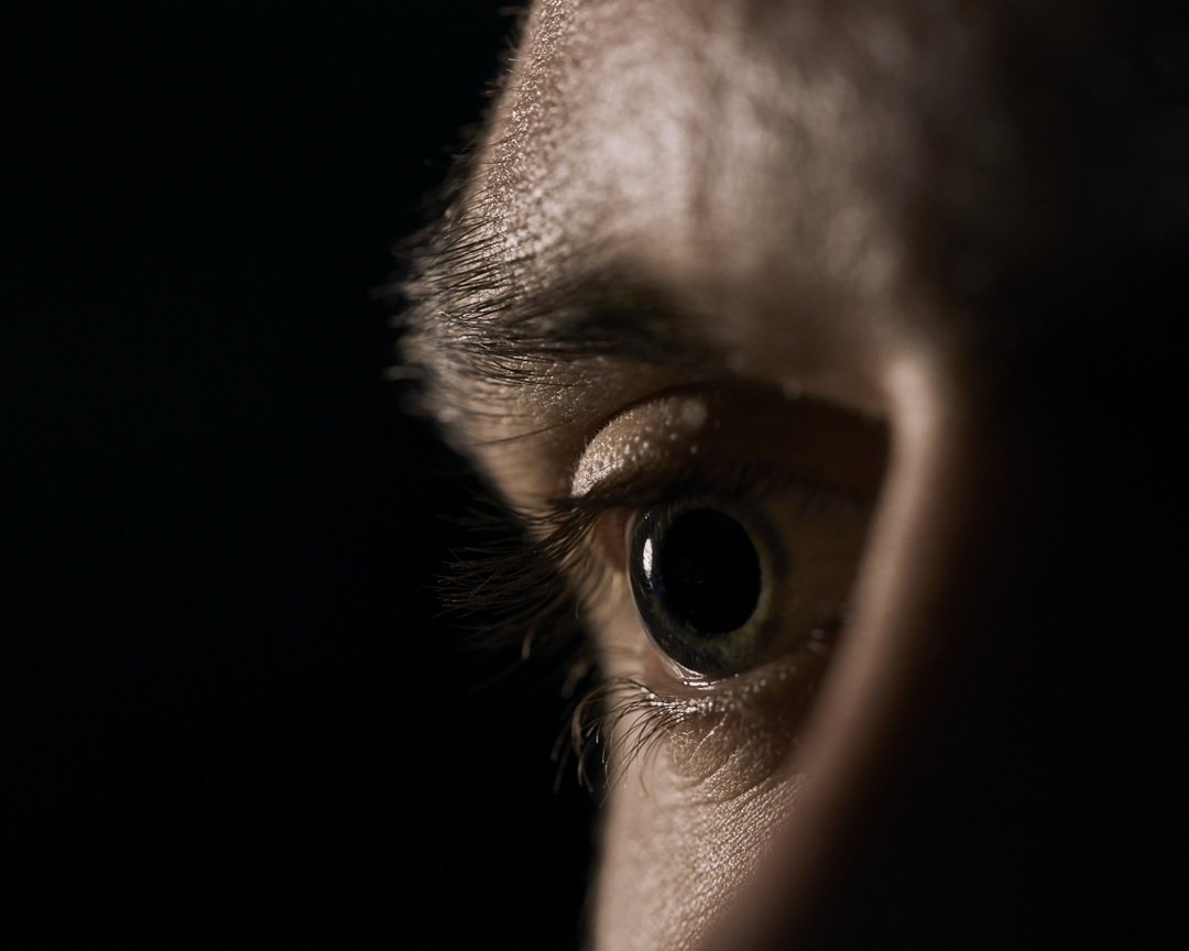 A closeup of a green human eye with dilated pupils on a black background